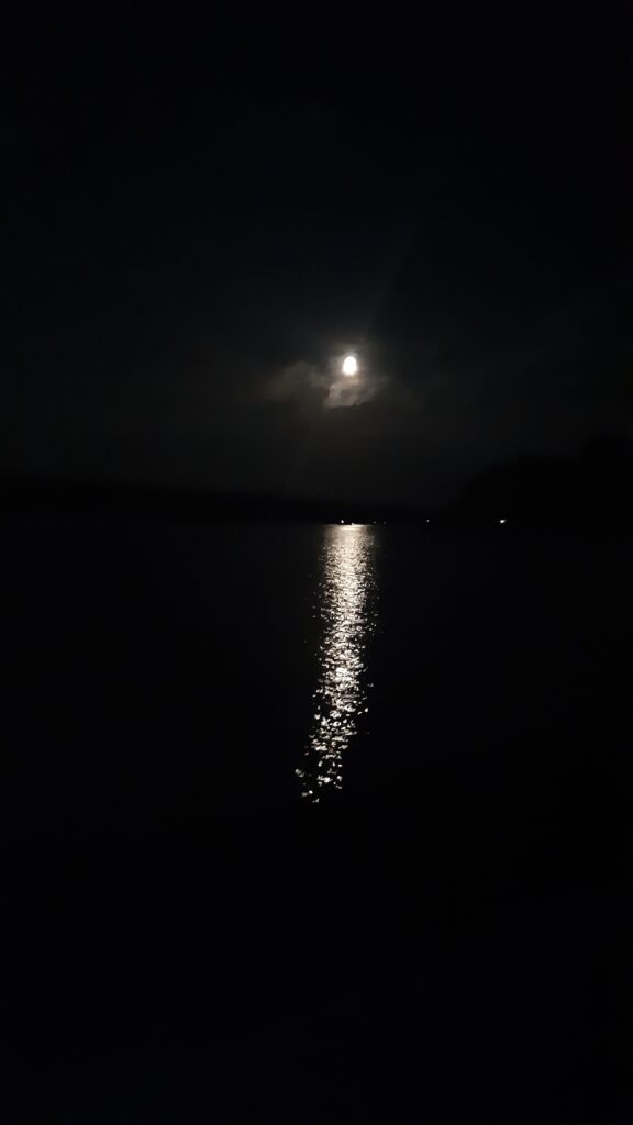 Fast voller Mond bei Nacht, mit glitzernder Schleppe auf der Wasseroberfläche